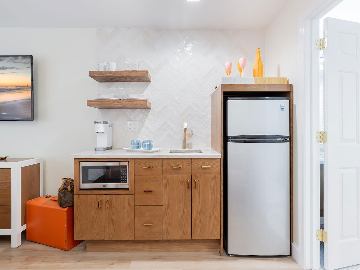 A small kitchenette with wooden cabinets, a microwave, a mini-fridge, and shelves featuring decor items like vases and glasses ends the sentence.