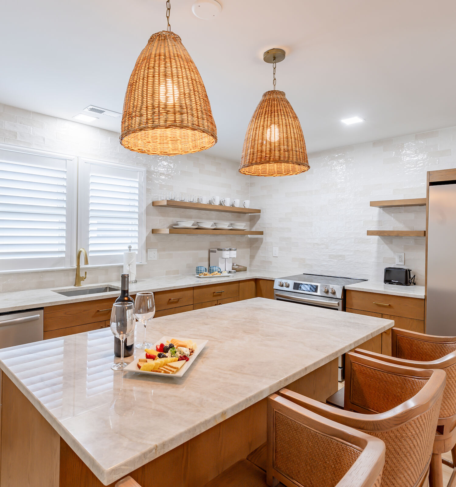A modern kitchen with wooden cabinets, a marble island with wicker chairs, stainless steel appliances, and pendant lighting.