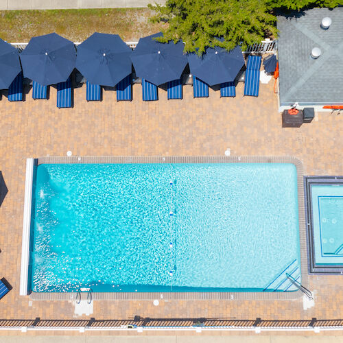 An aerial view of a swimming pool area with blue lounge chairs, umbrellas, and a smaller pool or hot tub adjacent to the main pool.
