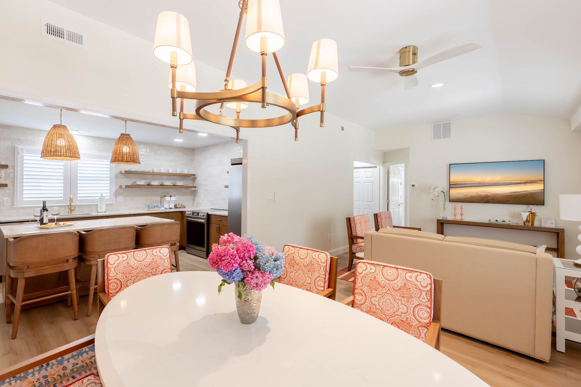 This image shows a modern open-concept living and dining area with a white oval dining table adorned with flowers and a cozy living room setup ending the sentence.