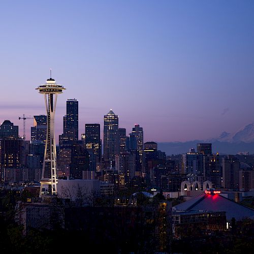 The image shows the Seattle skyline during twilight, featuring the Space Needle prominently, with Mount Rainier visible in the background.